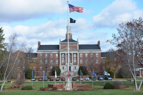 American and black flags on pole in front of large building.