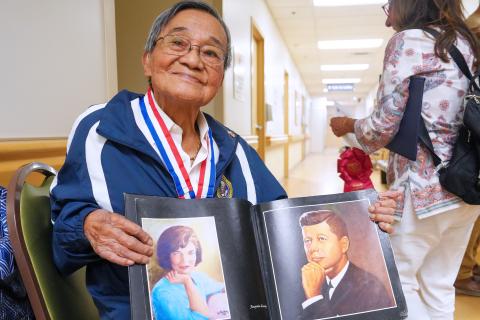 Veteran in blue jacket with medals, holding photo album.