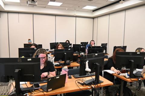 A group of people working at desks in an office with computers and laptops.