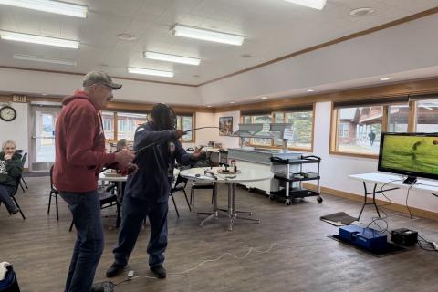 Two people enjoying a fishing similator in a room with a projector.screen.