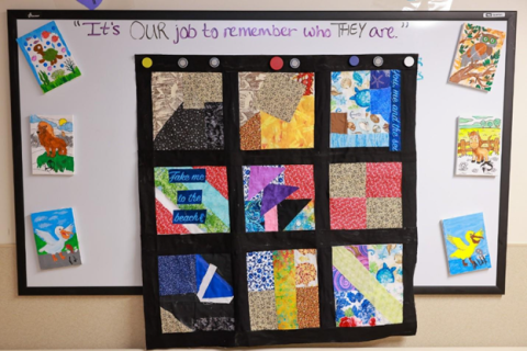 Patchwork quilt with various colors and shapes displayed on a bulletin board.