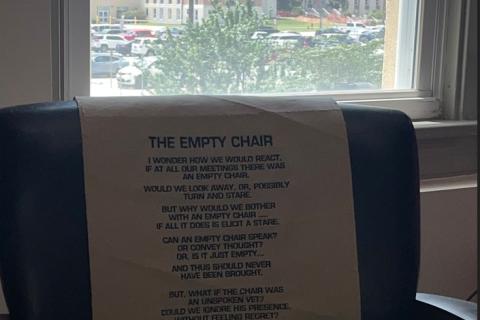 Office chair with "The Empty Chair" lyrics on backrest, window view of building behind.