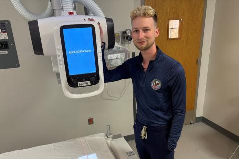 Man in blue scrubs standing next to a hospital bed with a medical device.