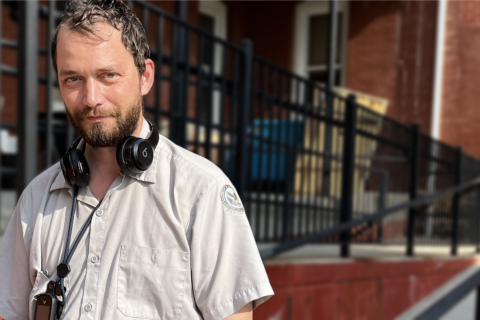 Man with headphones around his neck standing outside a brick building.