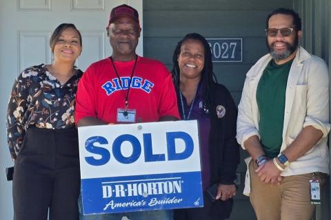 Four people stand by a door holding a "SOLD" sign.